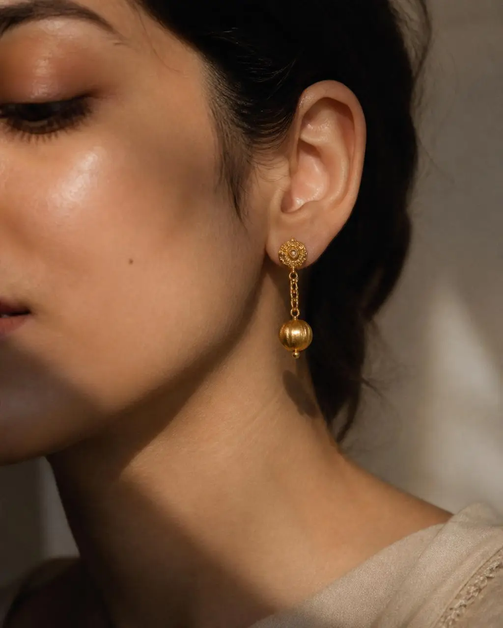Close-up of a handmade gold drop earring worn on the ear